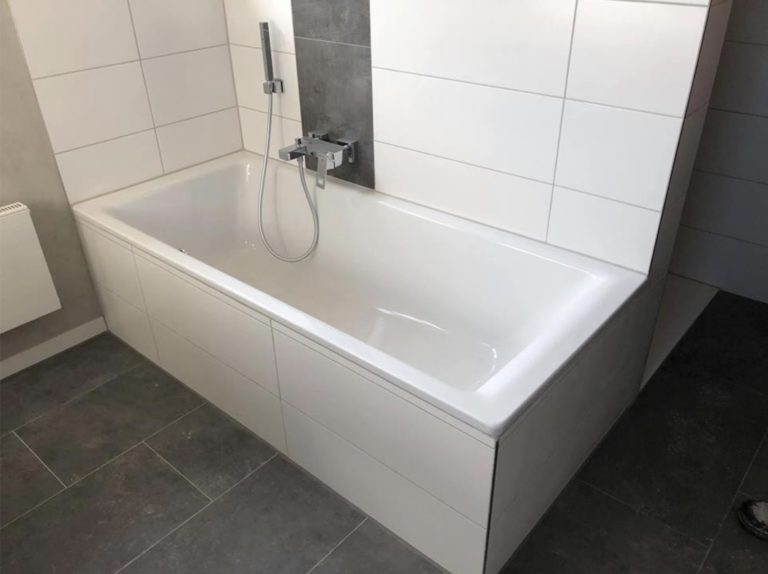 Weiße Badewanne mit Wandarmatur vor hell gefliester Wand
